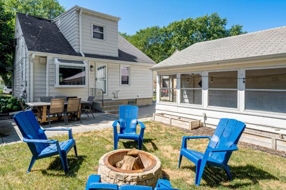 Backyard fire pit ringed with blue Adirondack chairs between the house and garage