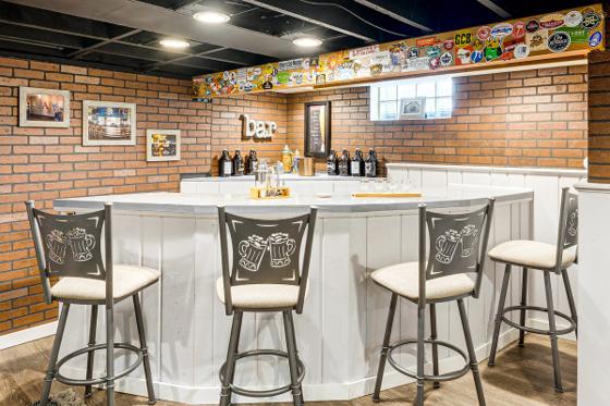 Finished basement bar with exposed brick, four swivel barstools and a stocked back counter