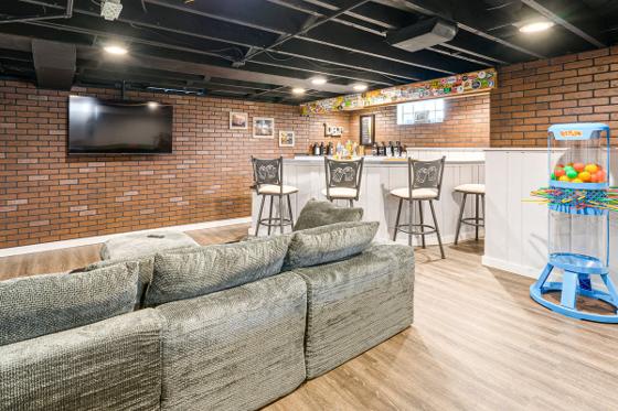 Basement lounge with a large sectional facing a wall-mounted television, bar behind