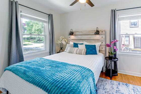 Sunny bedroom with windows on two walls, a reclaimed wood headboard and teal accents
