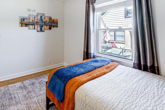 Bedroom with a curtained window, layered blue and orange throws and city skyline art