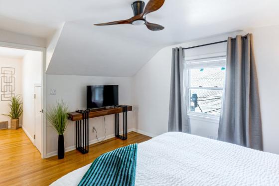 Upstairs bedroom under a sloped ceiling with a wall-mounted television and ceiling fan