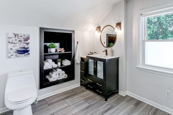 Full bathroom with a black vanity, round mirror and a recessed shelving niche