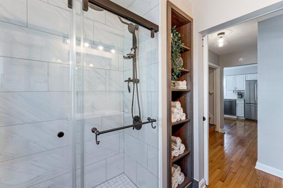 Marble-tiled walk-in shower with a sliding glass door and built-in towel shelving