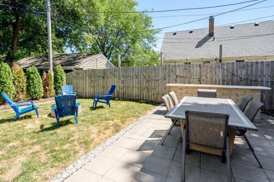 Paver patio with a six-seat dining table beside a fenced lawn and Adirondack chairs