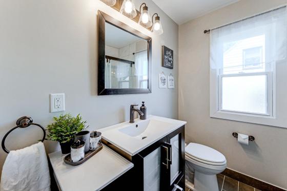 Powder room with a dark vanity, framed mirror and a window over the toilet