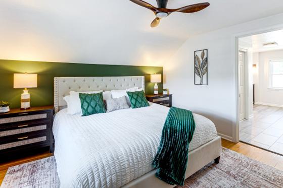 Primary bedroom with a deep green accent wall, upholstered headboard and ceiling fan