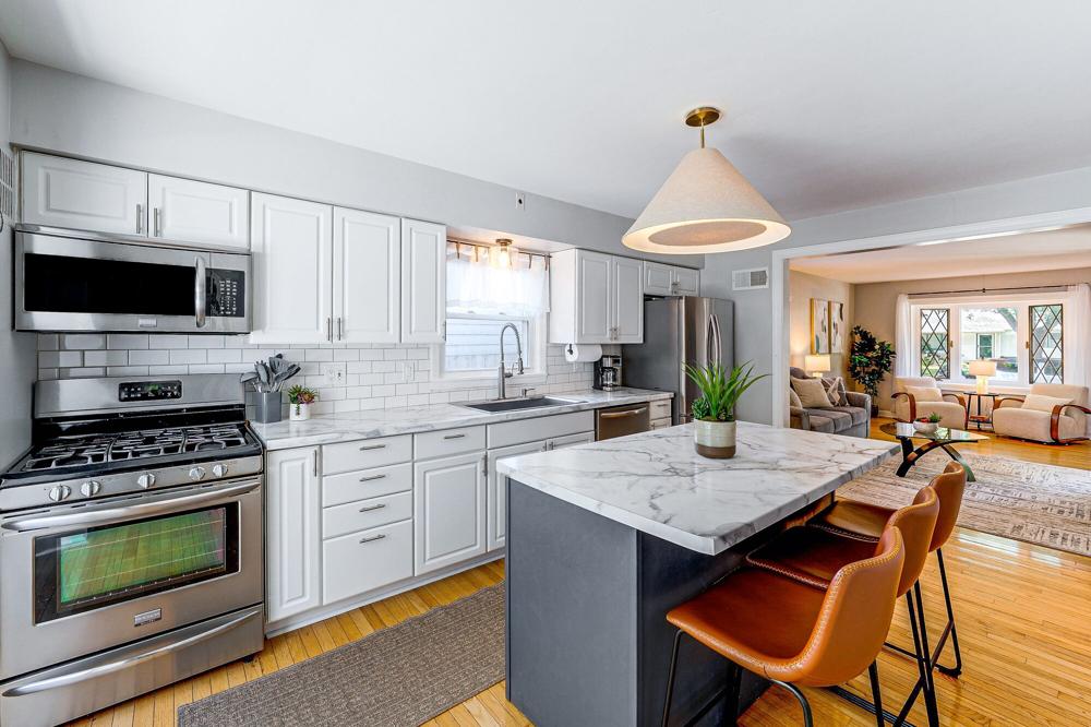 Renovated kitchen with white shaker cabinets, subway tile and a marble-topped island opening onto the living room